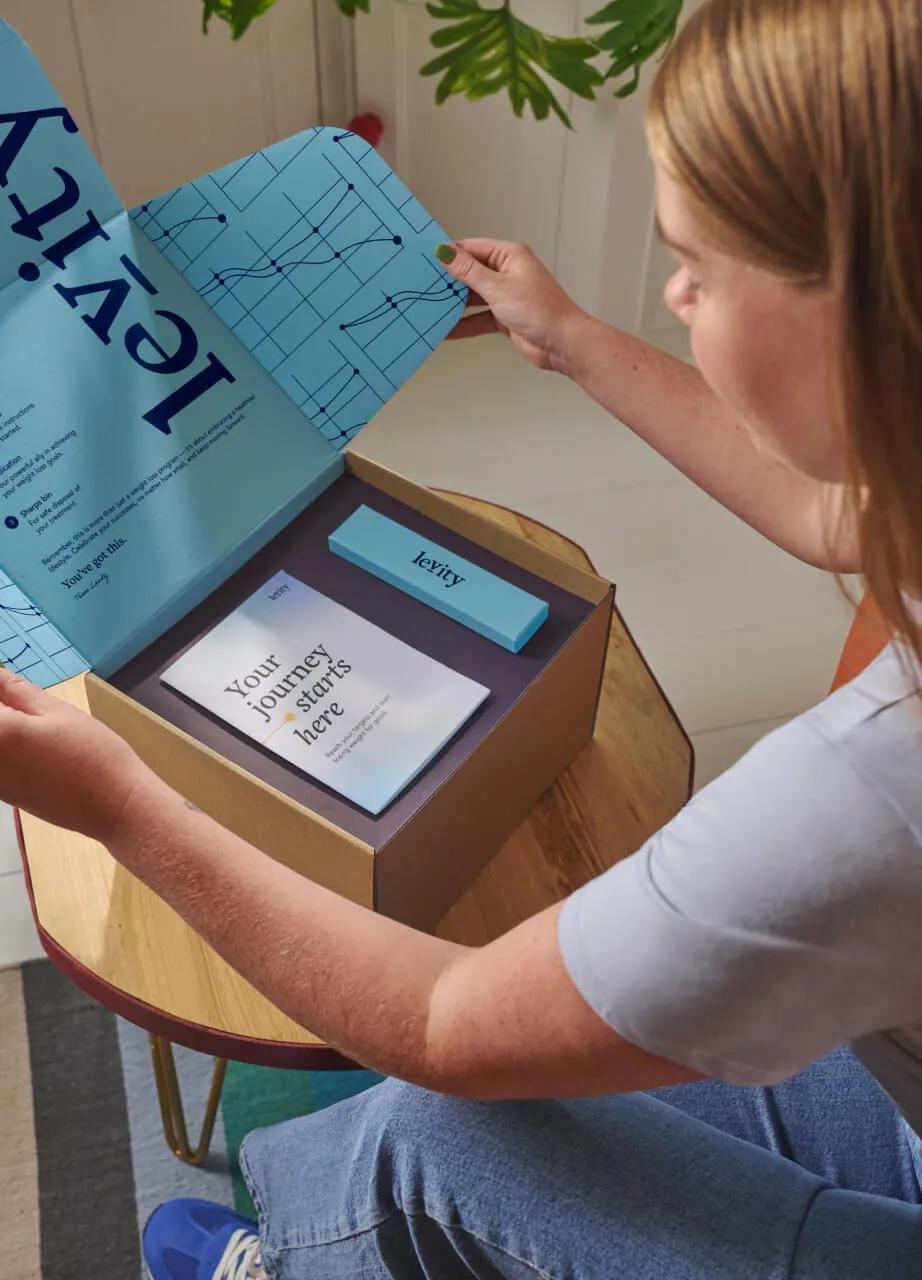 Woman unboxing a Levity package containing a leaflet with the title 'Your journey starts here'