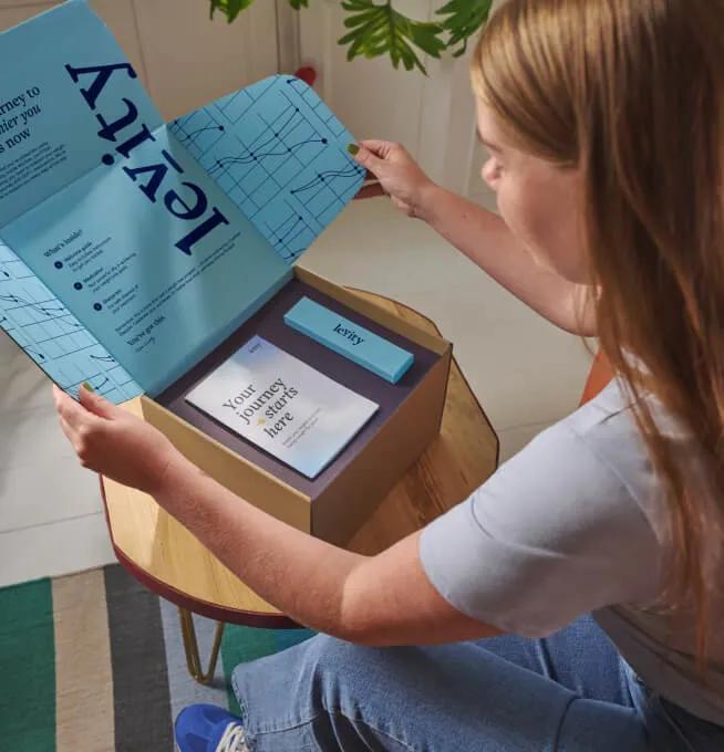 Woman unboxing a Levity package containing a leaflet with the title 'Your journey starts here'