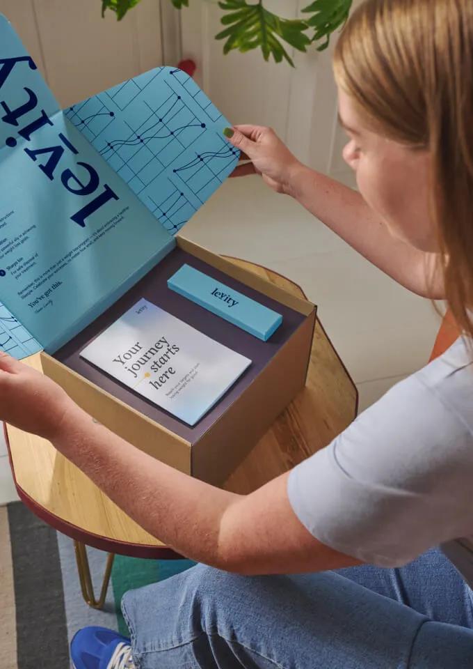 Woman unboxing a Levity package containing a leaflet with the title 'Your journey starts here'